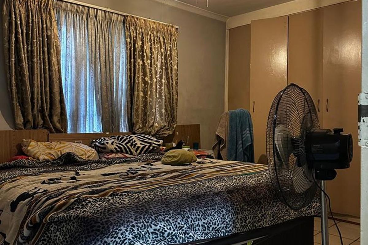 A bedroom featuring tiled flooring, a ceiling fan, and built-in cupboards, offering a functional space with standard finishes.