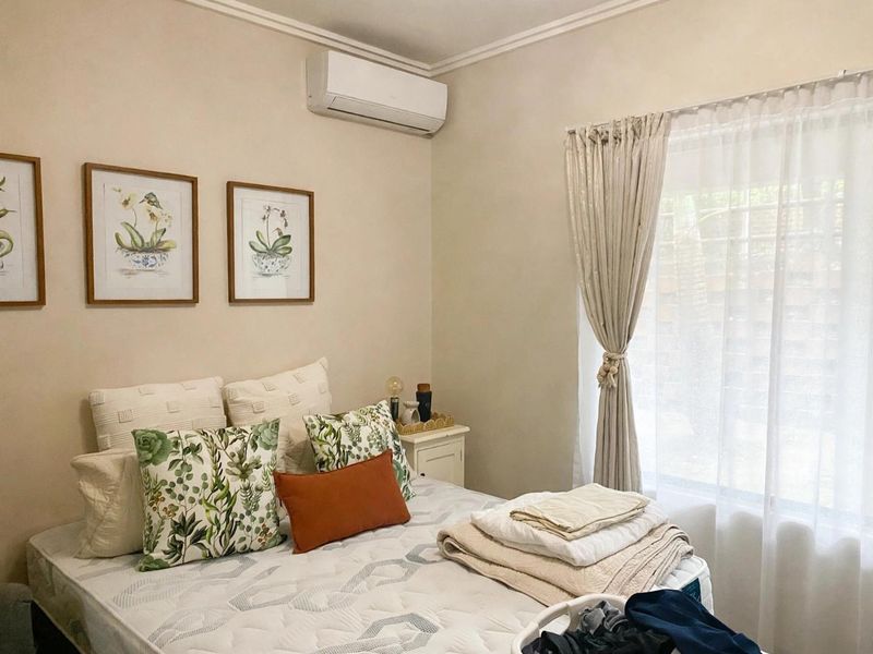 A well-maintained bedroom featuring a wall-mounted split-system air conditioner, neutral wall finishes, and natural light through window curtains.