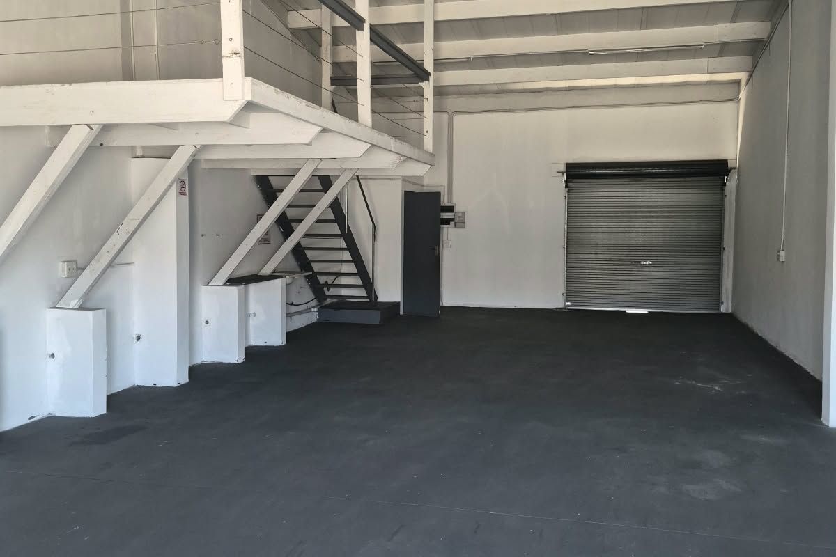 Spacious industrial utility area featuring a mezzanine level, metal staircase, roller shutter door, and exposed timber rafters with durable concrete flooring.