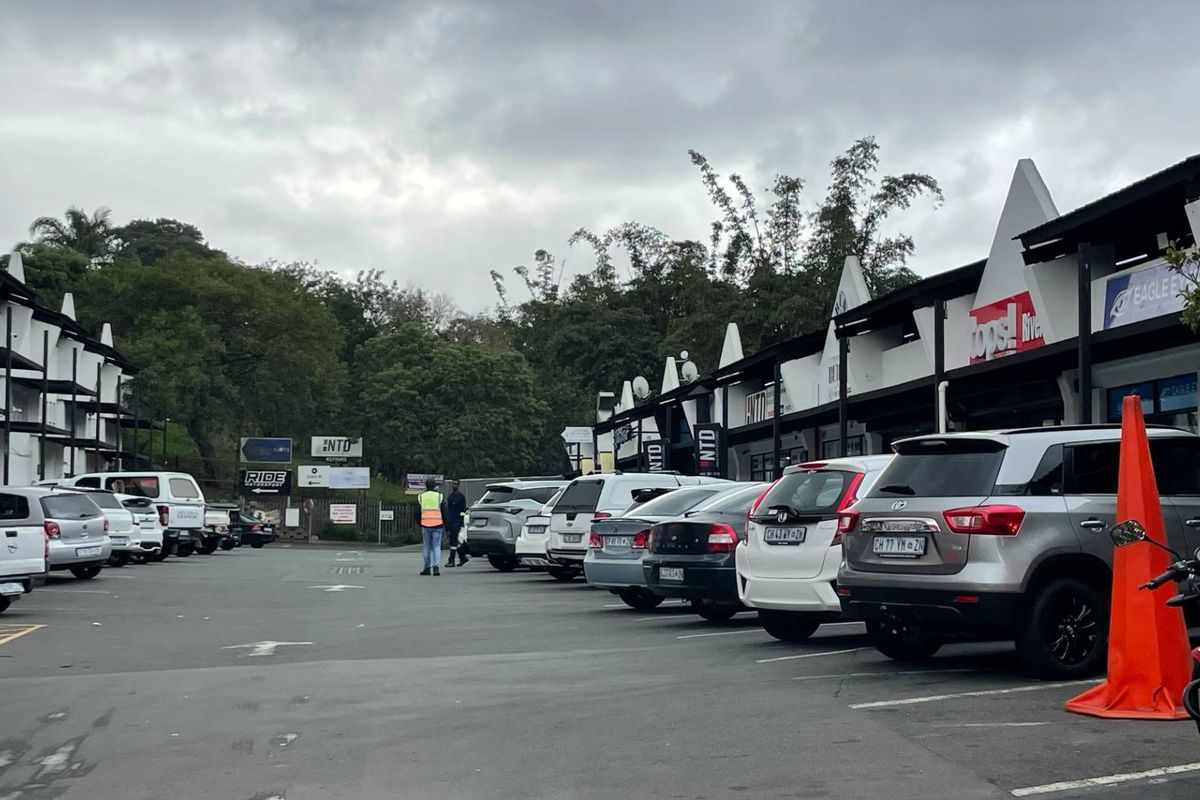 A view of a retail center parking lot with storefronts and covered walkways.