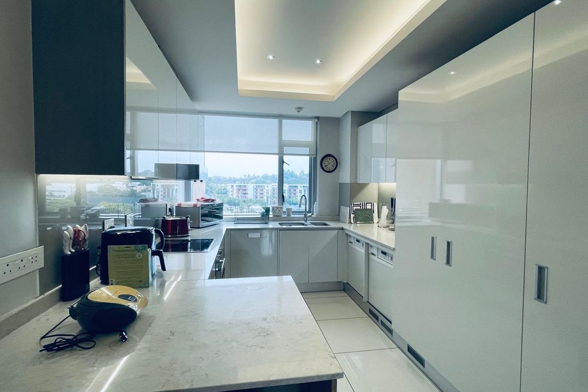 Modern kitchen featuring sleek white cabinetry, stone countertops, integrated appliances, and recessed ceiling lighting with a large window providing natural light and views.