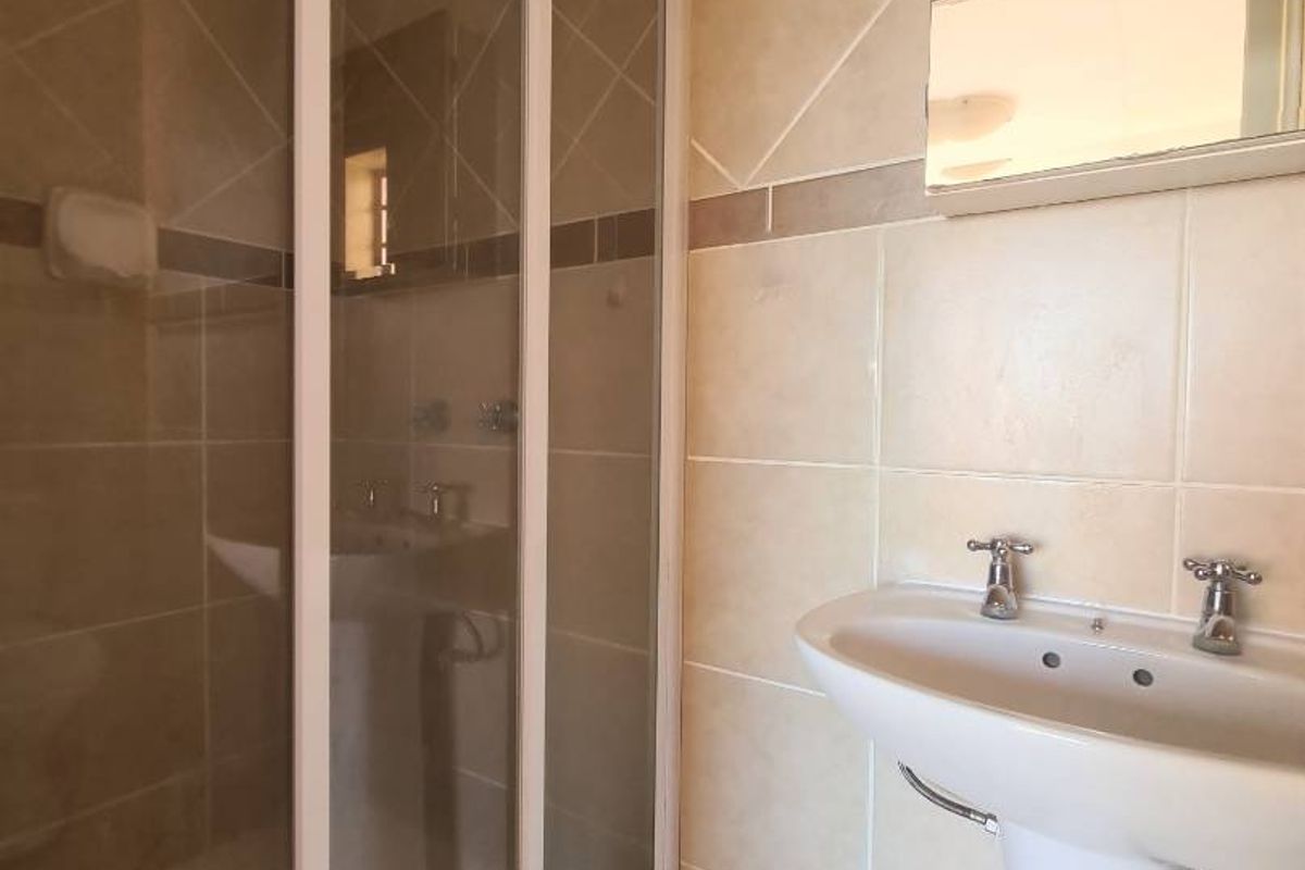 A functional bathroom featuring a pedestal sink, a glass-enclosed shower, and neutral wall tiling.