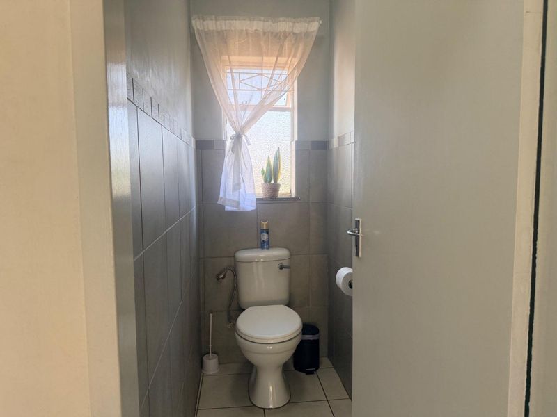 A compact guest bathroom featuring neutral ceramic wall and floor tiling, a standard toilet, and a window with security bars.