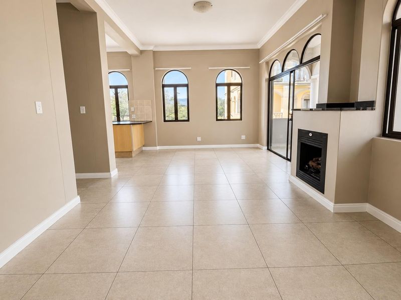 Spacious open-plan living area featuring tiled floors, a built-in fireplace, arched windows, and direct access to an outdoor patio area.