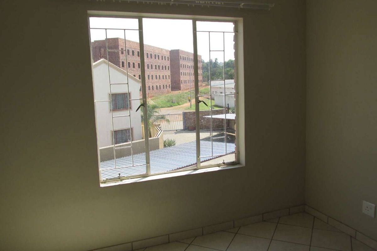 An empty bedroom featuring tiled flooring, a window with security bars, and a curtain rail, offering a view of the surrounding apartment complex.