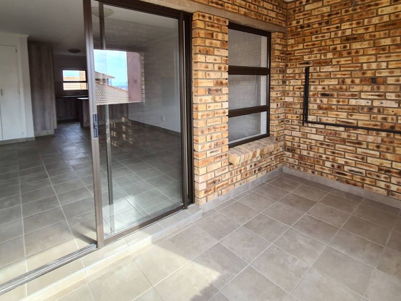 A covered balcony featuring exposed brick walls and tiled flooring, providing a seamless transition to the interior living space through large sliding glass doors.