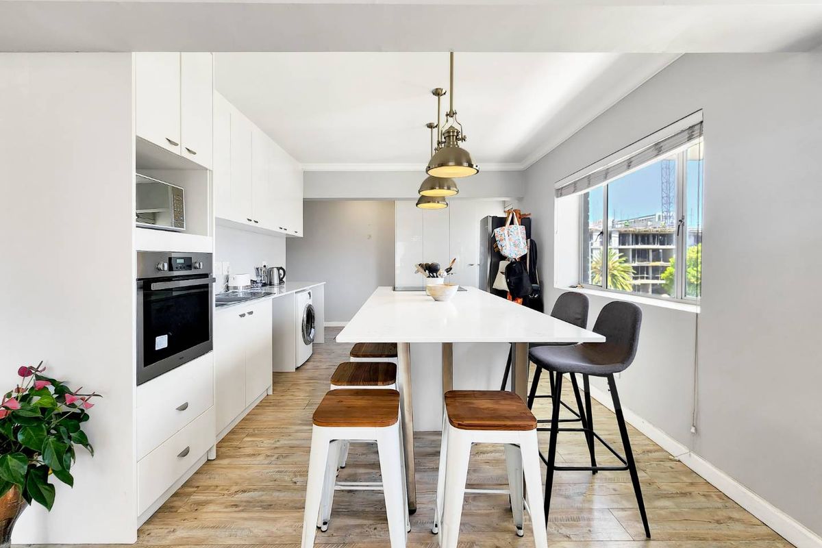 Modern kitchen featuring white cabinetry, a central island with breakfast bar seating, built-in oven, microwave, and integrated laundry appliances.