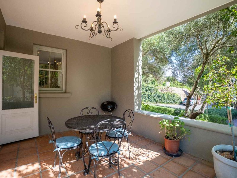 A covered patio featuring terracotta floor tiles, a classic wrought iron chandelier, and direct access to the garden through a white french door.