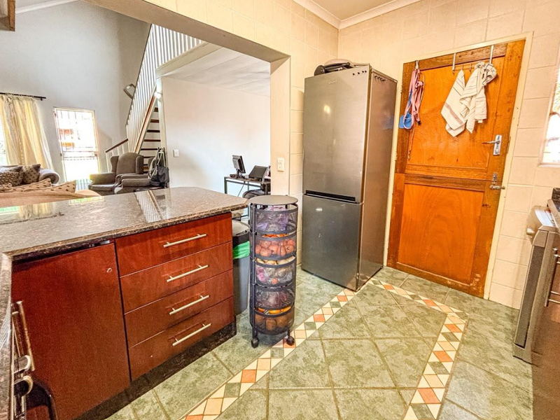 Kitchen area featuring granite countertops, wooden cabinetry, and tiled flooring, with an open-plan layout connecting to the living space and staircase.