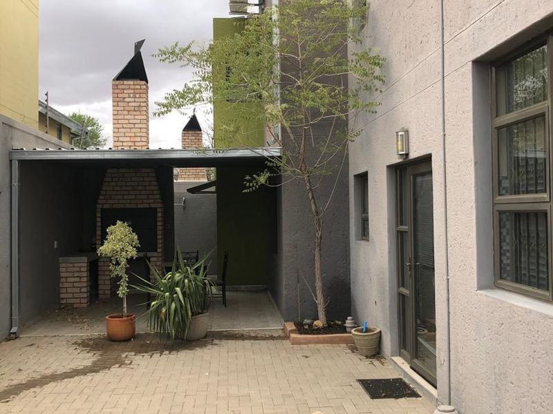 Rear courtyard featuring a paved patio area with a built-in brick braai and covered entertainment space.