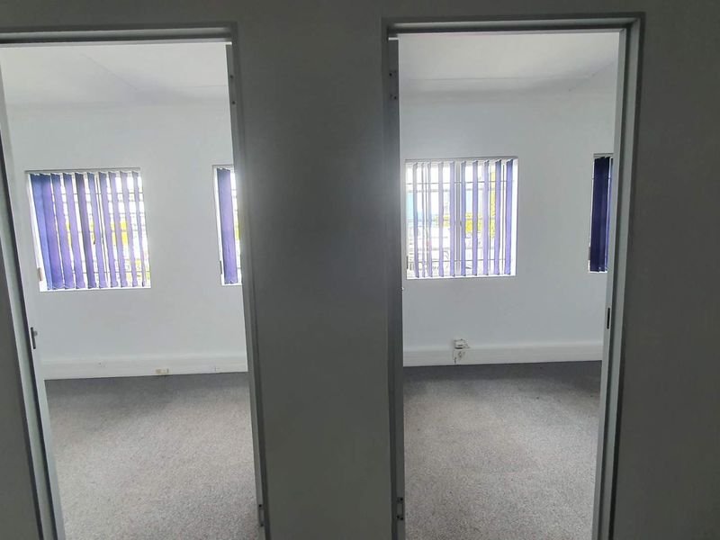 Two adjacent vacant office spaces featuring neutral walls, carpeted flooring, and vertical window blinds, providing a clean and functional workspace environment.