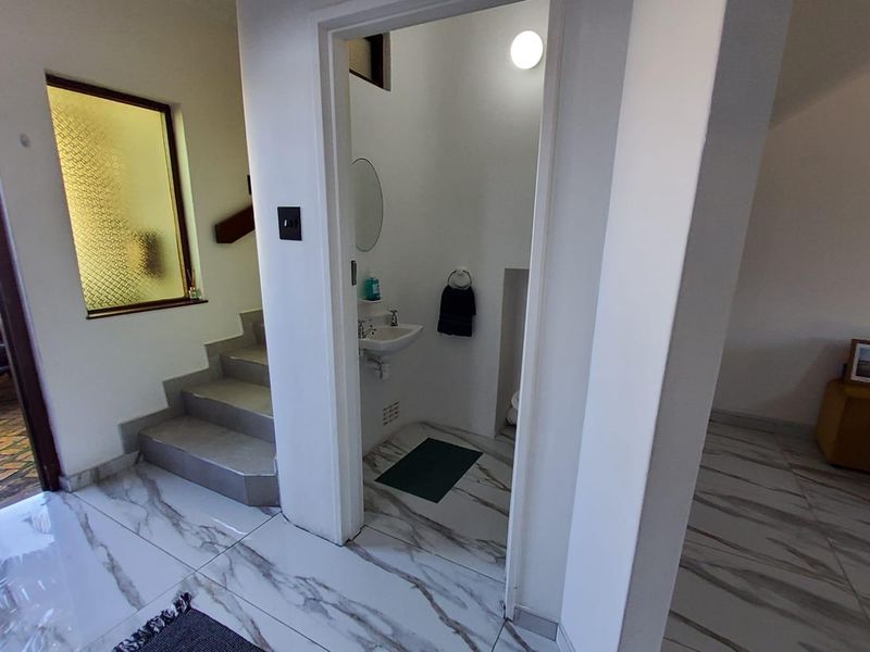 A compact guest bathroom featuring a wall-mounted basin and toilet, situated adjacent to a tiled staircase area in the townhouse.