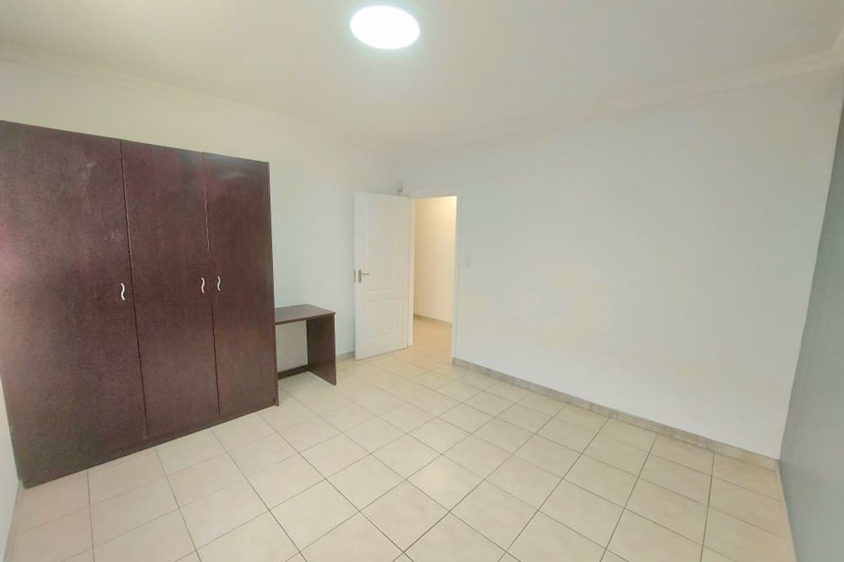 A clean, empty bedroom featuring neutral tiled flooring and a large built-in wardrobe, offering a blank canvas for personalization.