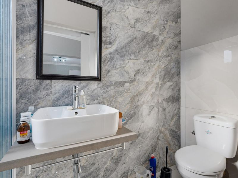 Modern bathroom featuring a vessel sink on a wall-mounted shelf, chrome fixtures, and elegant marble-effect wall tiling.