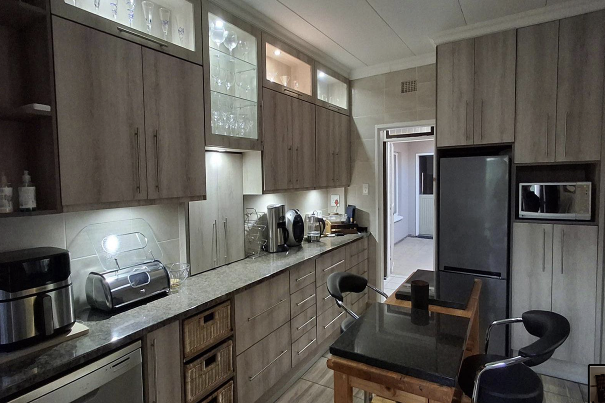 Modern kitchen featuring wood-grain cabinetry, stone countertops, integrated lighting, and a breakfast nook area with direct access to an adjacent hallway.