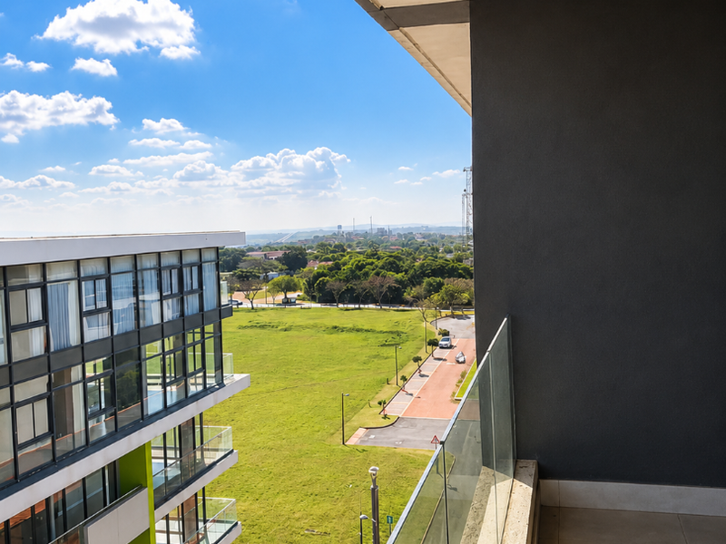 A modern apartment balcony featuring a sleek glass balustrade, tiled flooring, and expansive views over the surrounding landscape and neighboring buildings.