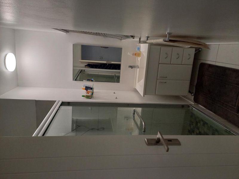 A compact bathroom featuring a glass shower enclosure, a modern vanity unit with basin, and a wall-mounted mirror.
