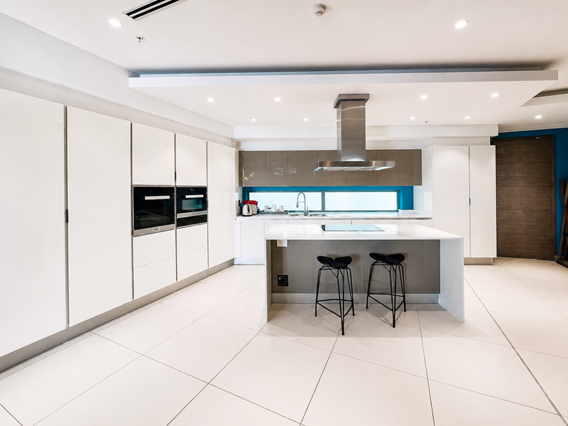 Modern, high-end kitchen featuring sleek white cabinetry, a central island with an integrated hob, built-in appliances, and polished tile flooring.