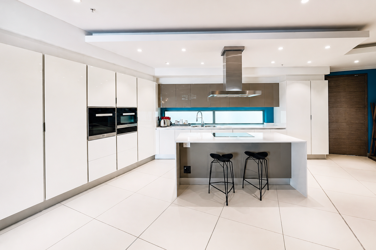 Modern, high-end kitchen featuring sleek white cabinetry, a central island with an integrated hob, built-in appliances, and polished tile flooring.