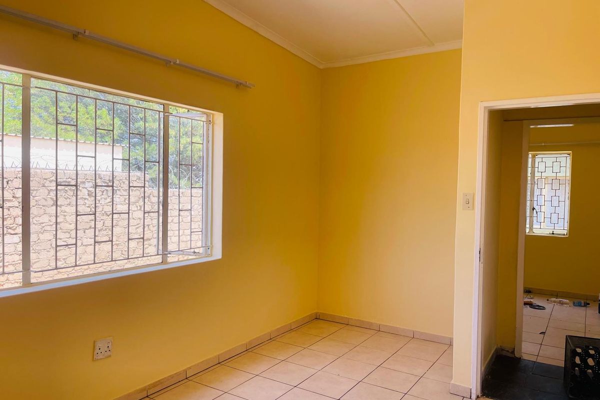 An empty living area featuring tiled flooring, yellow walls, and security bars on the windows, leading into an adjacent room.