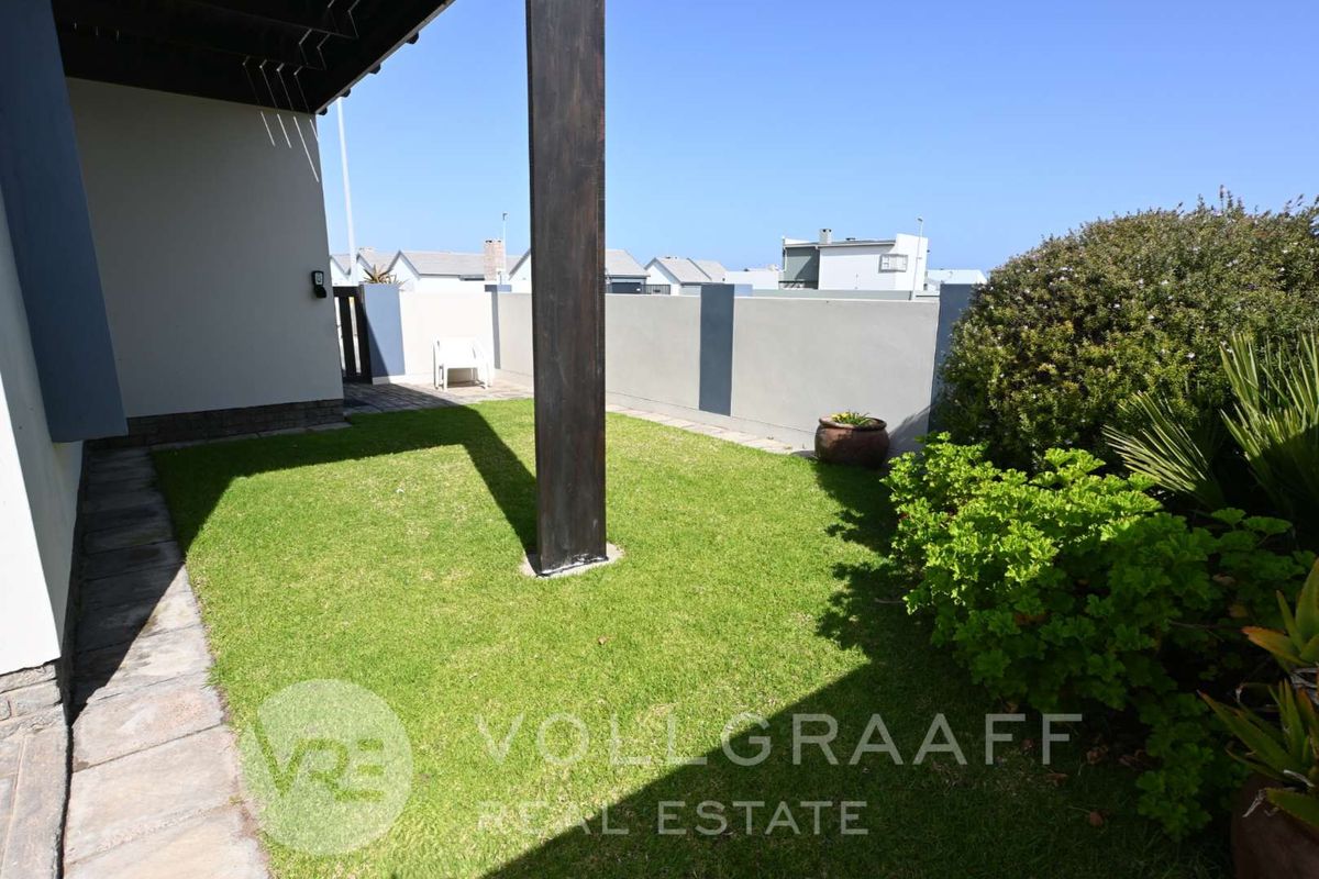A private rear garden area featuring a manicured lawn, perimeter boundary walls, and a covered patio section with a structural support pillar.