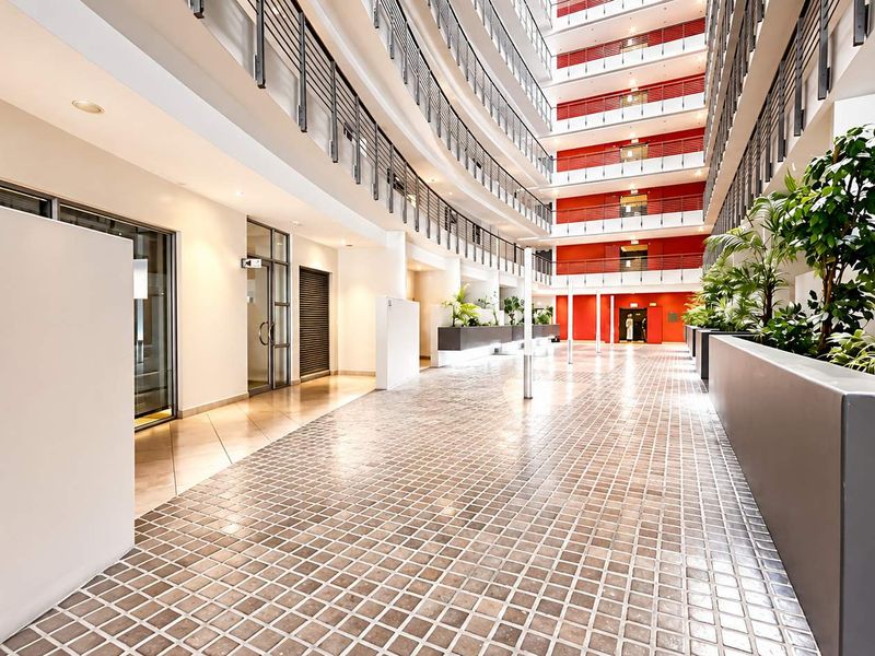 A spacious, well-maintained indoor atrium or communal area featuring tiled flooring, modern metal railings, and integrated planters within an apartment complex.