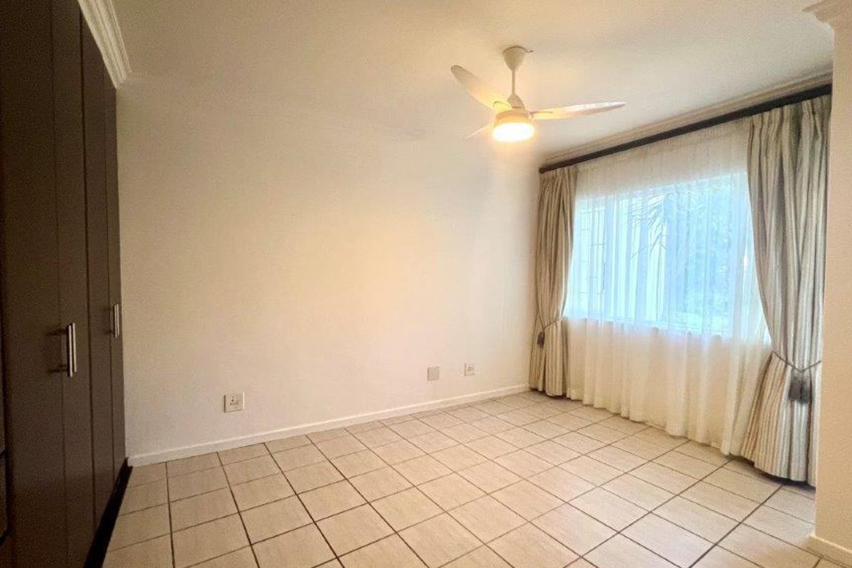 A spacious, empty bedroom featuring tiled flooring, built-in cupboards, and a ceiling fan, offering a clean canvas for personalization.
