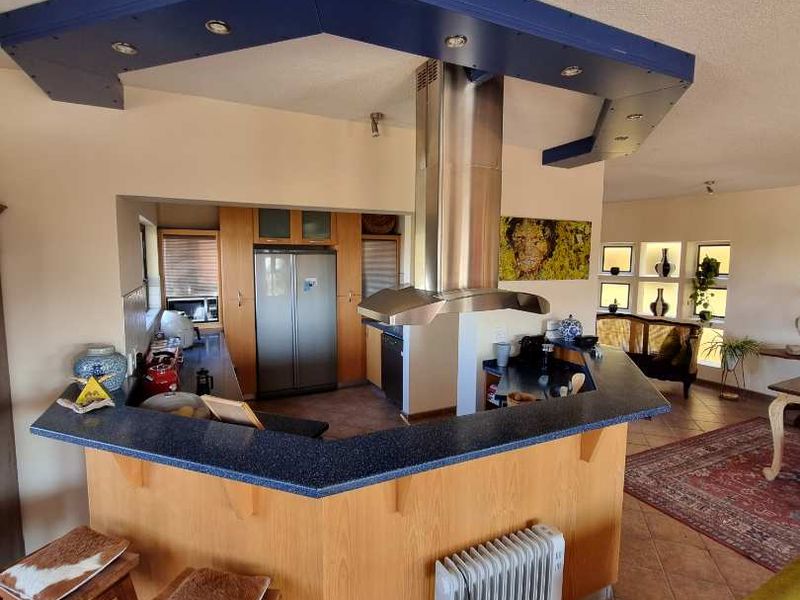Open plan kitchen featuring a central island with a stainless steel extractor fan, stone countertops, and built-in cabinetry, flowing into the living area.