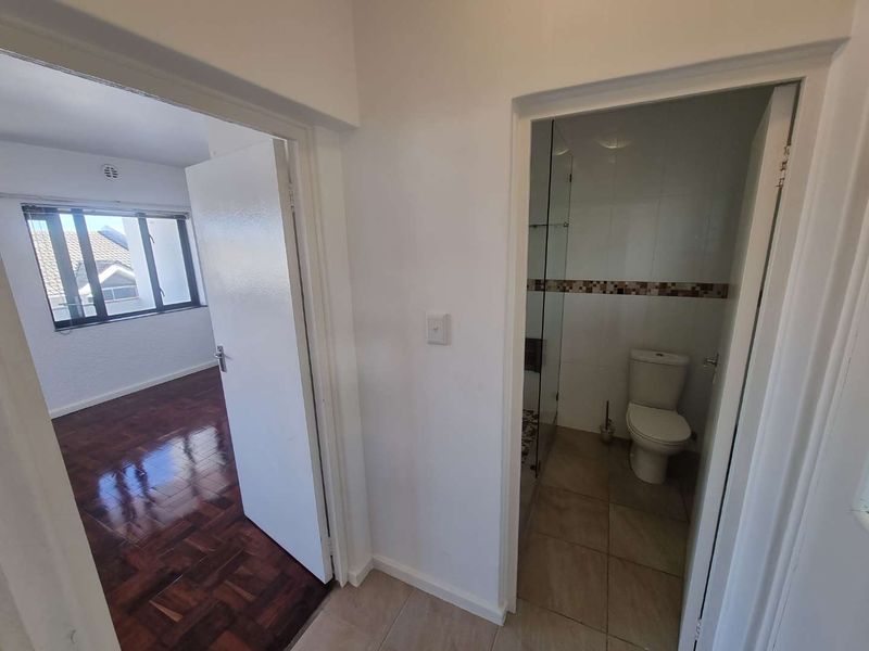 A view from the hallway looking into a bedroom with parquet flooring and an adjacent bathroom featuring a toilet and glass shower enclosure.