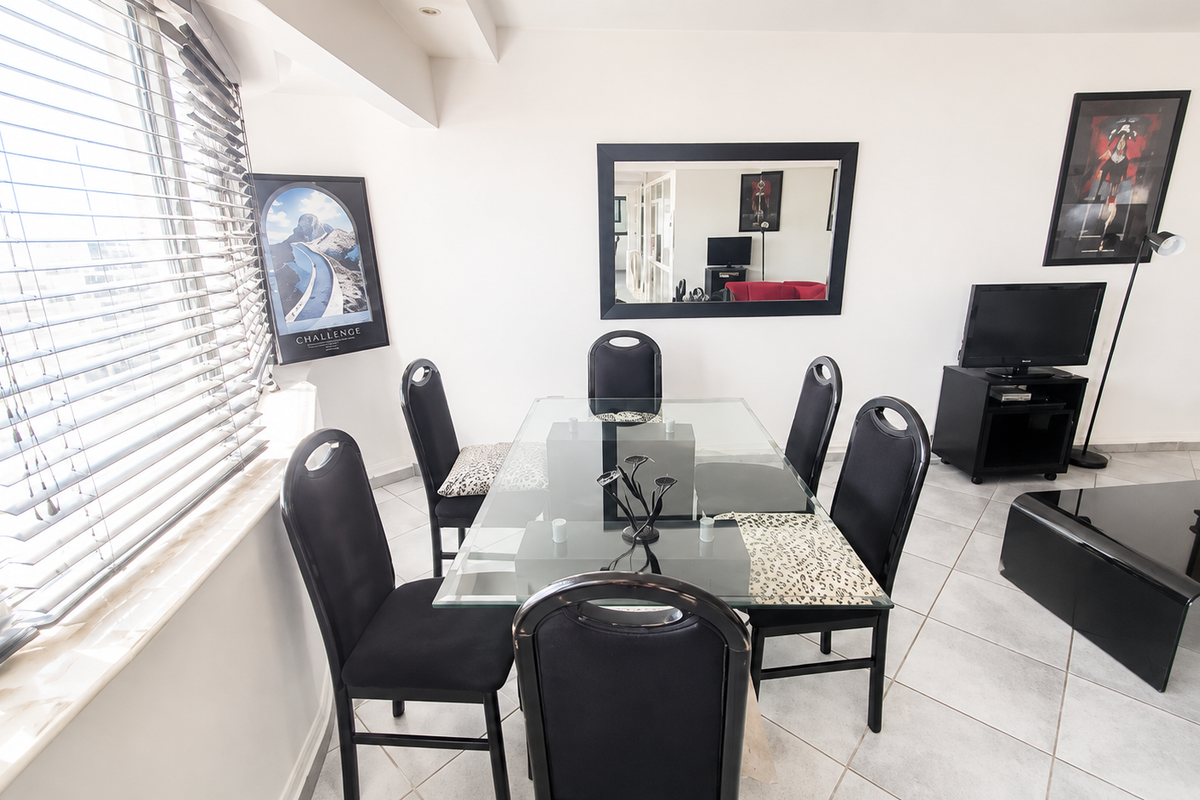 A bright living and dining area featuring neutral tiled flooring, large windows with venetian blinds, and recessed ceiling lighting.