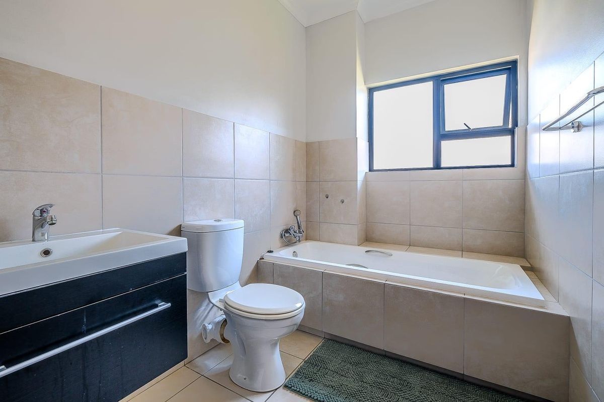 A functional bathroom featuring a built-in bathtub, a modern vanity with a basin, and a standard toilet, finished with neutral wall tiles.