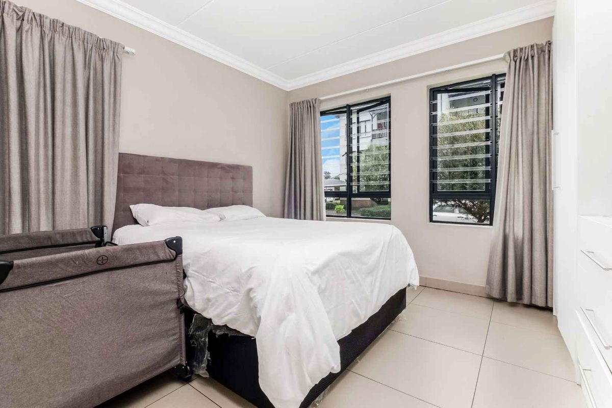 A bright bedroom featuring tiled flooring, built-in cupboards, and large windows with security louvers, providing ample natural light.
