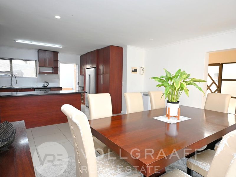 Open-plan dining area featuring tiled flooring and recessed lighting, seamlessly connected to a functional kitchen with dark wood cabinetry and stone countertops.