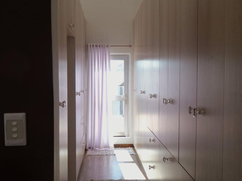 A well-lit hallway featuring extensive floor-to-ceiling built-in cabinetry, laminate flooring, and a glass panel door leading to an outdoor area.