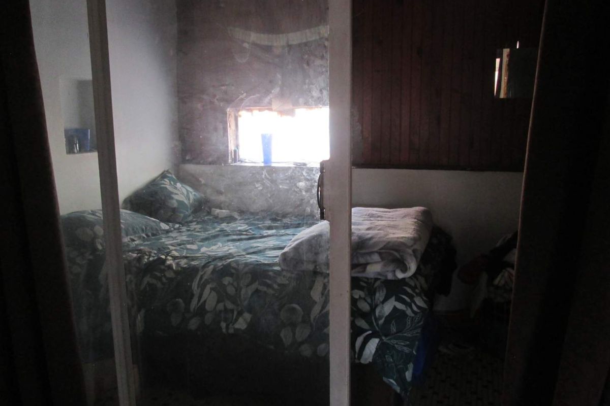 A bedroom featuring timber wall paneling and a built-in wardrobe, currently showing significant signs of wear and requiring cosmetic refurbishment.