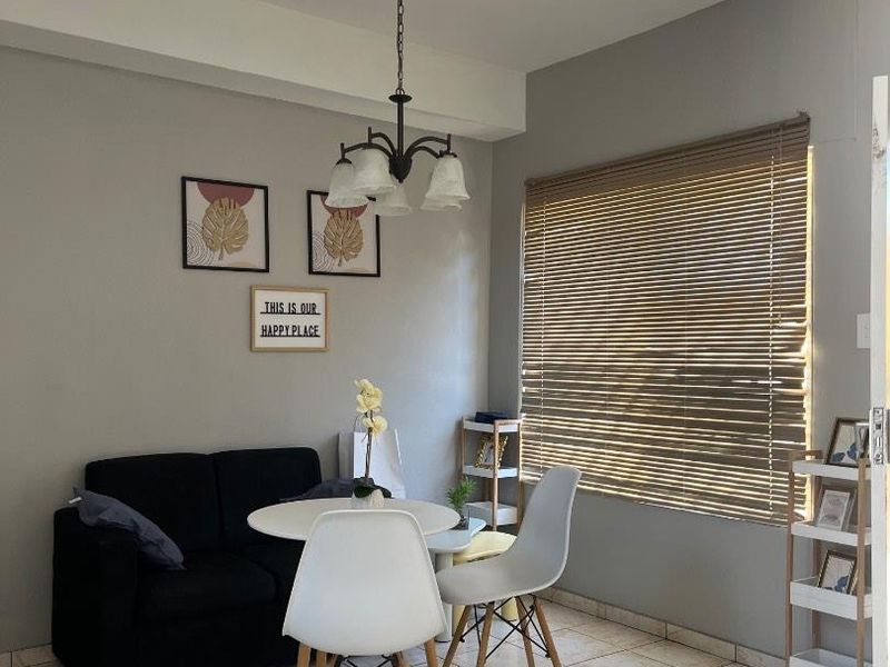 A bright living area featuring ceramic tile flooring, a central pendant light fixture, and venetian blinds allowing natural light into the space.
