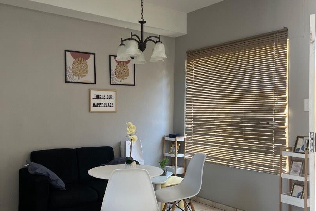 A bright living area featuring ceramic tile flooring, a central pendant light fixture, and venetian blinds allowing natural light into the space.