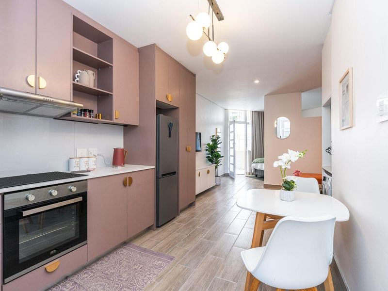 Modern open-plan kitchen and living area featuring contemporary mauve cabinetry, integrated appliances, and sleek tiled flooring leading to an adjacent bedroom space.