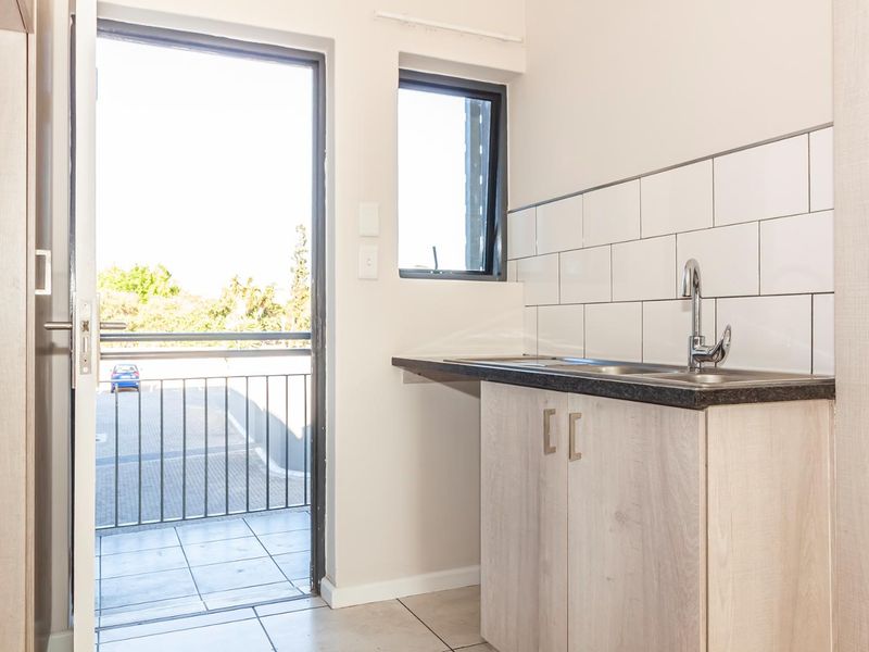 A clean, functional scullery area featuring modern cabinetry, a stainless steel sink with subway tile backsplash, and direct access to an outdoor balcony.