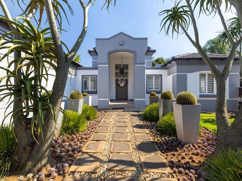 A well-maintained front entrance featuring a stone paver walkway leading to a covered portico, framed by landscaped garden beds and mature trees.