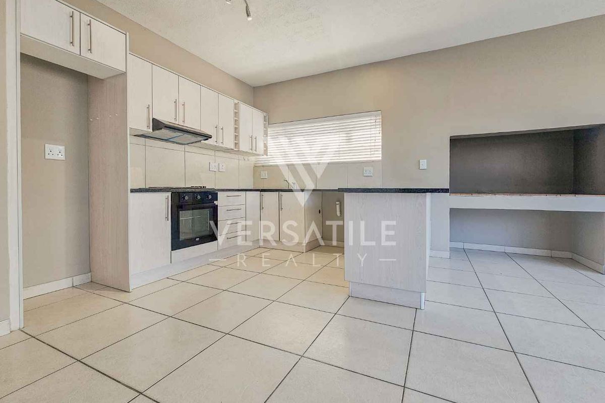 Modern kitchen featuring white cabinetry, built-in oven, extractor fan, and a convenient indoor braai area, finished with neutral tiled flooring.