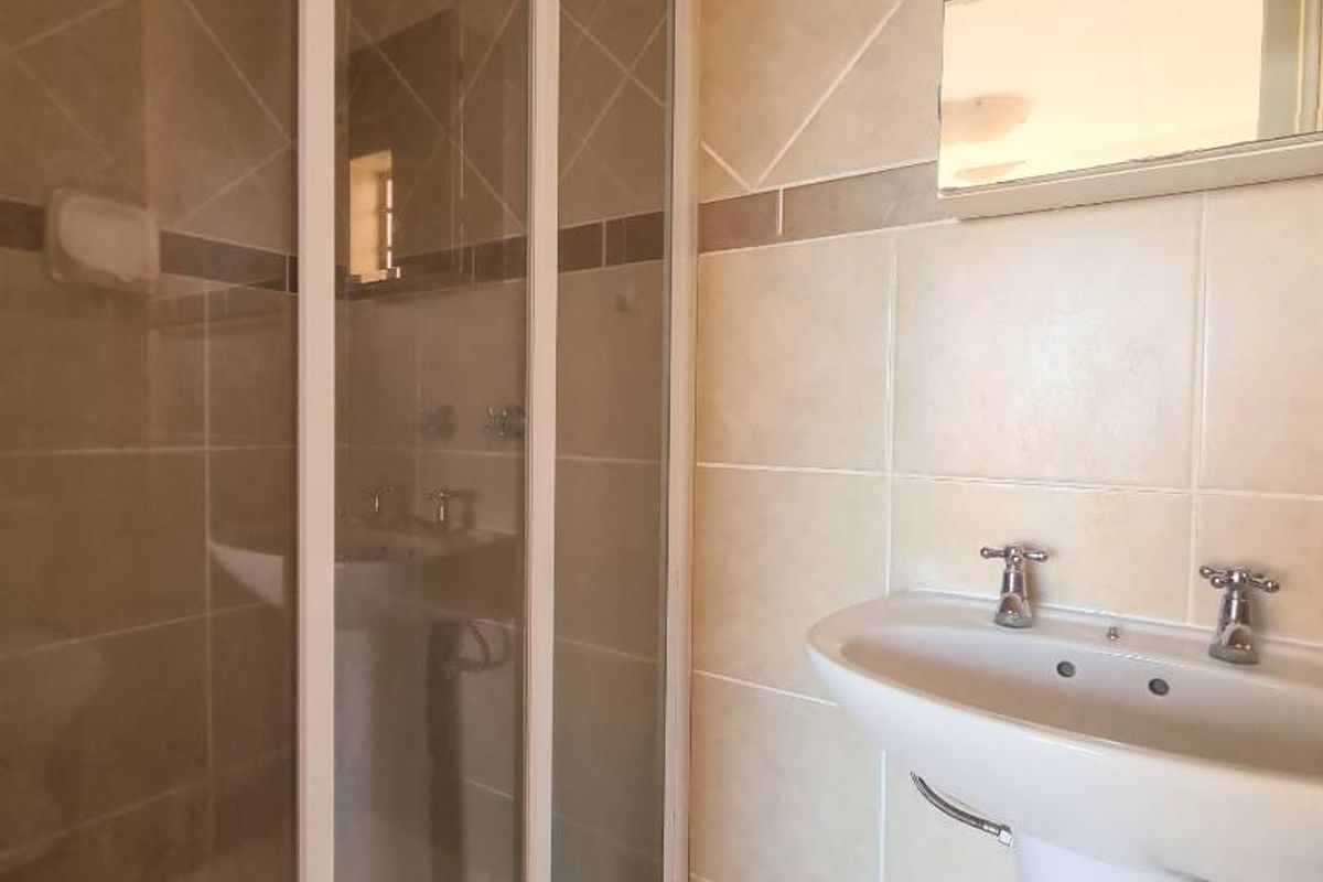 A functional bathroom featuring a pedestal sink, a glass-enclosed shower stall, and neutral wall tiling.