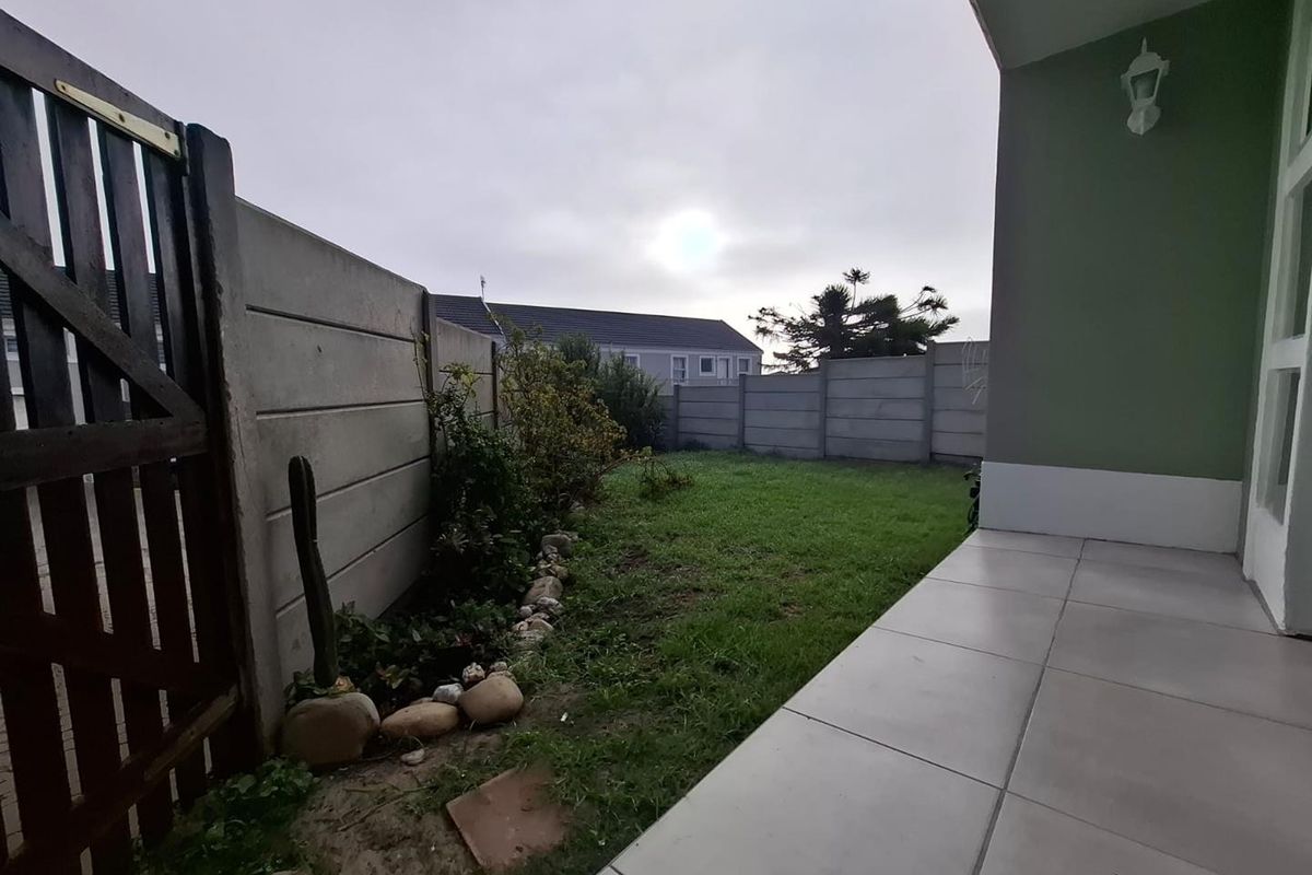 A private rear garden featuring a tiled patio area, lawn, and concrete boundary walling, providing a functional outdoor space.