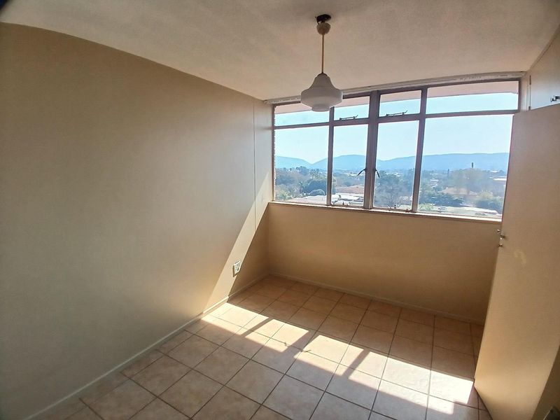 An empty bedroom featuring tiled flooring, a large window with scenic views, and a built-in cupboard, offering a blank canvas for personalization.
