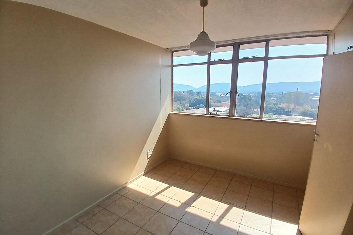 An empty bedroom featuring tiled flooring, a large window with scenic views, and a built-in cupboard, offering a blank canvas for personalization.