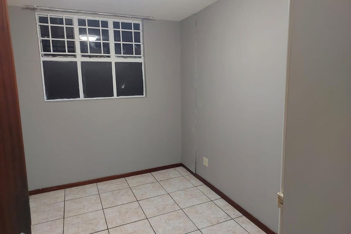 An empty bedroom featuring tiled flooring, a window with security bars, and neutral grey walls.