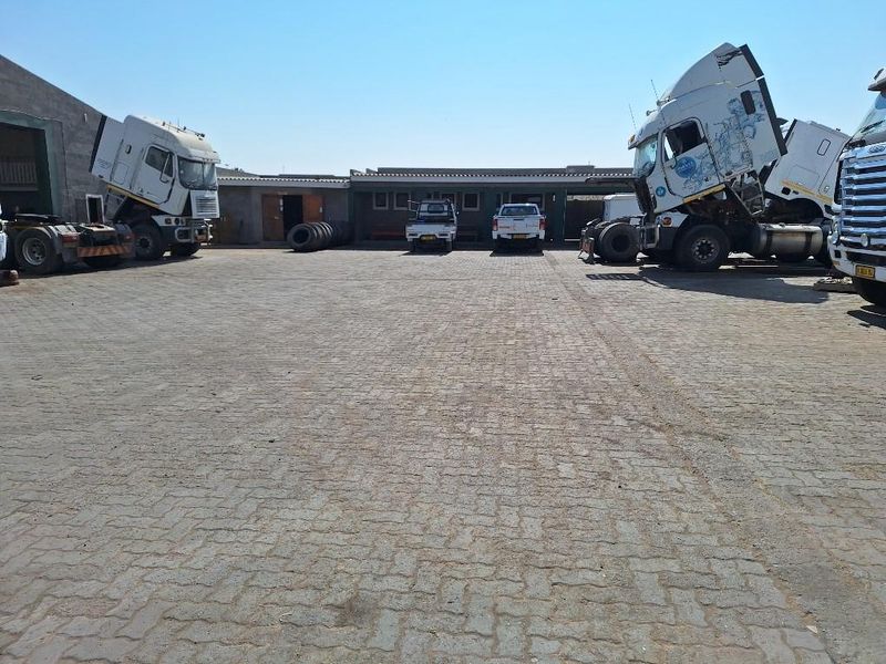 Spacious industrial yard with paved surface and access to warehouse buildings, suitable for heavy vehicle parking and logistics operations.