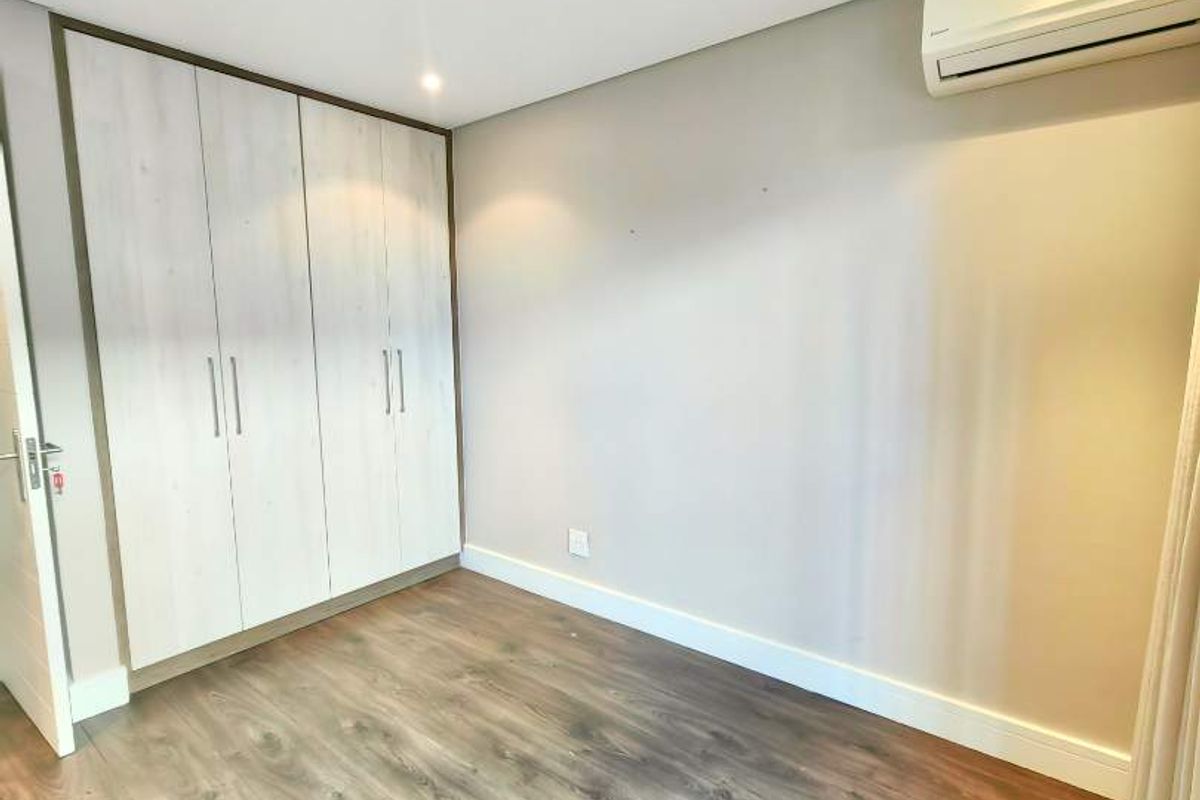 A bright, empty bedroom featuring modern laminate flooring, built-in cupboards, and a wall-mounted air conditioning unit.