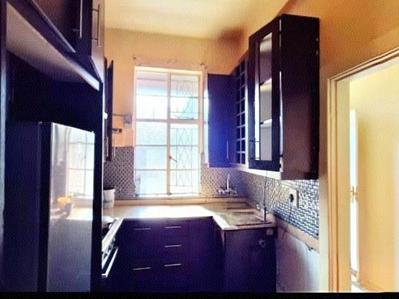 A compact kitchen featuring dark wood cabinetry, mosaic tile backsplash, and a window with security bars, requiring minor finishing work to the lower wall area.