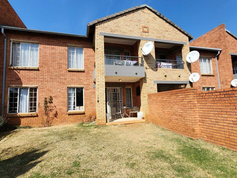 Rear view of a face brick apartment complex featuring private balconies, security gates, and a small private garden area.
